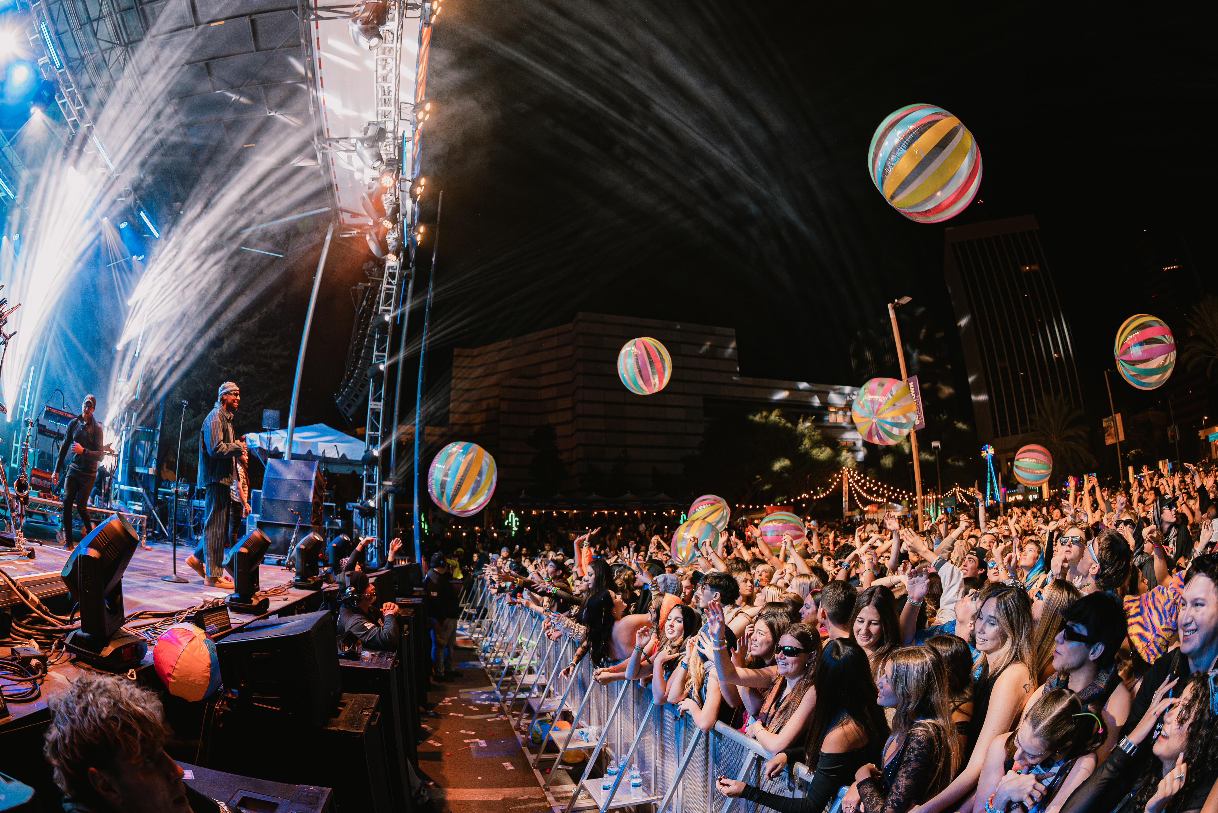 A large DUSK festival crowd reaching toward beach balls under stage lights