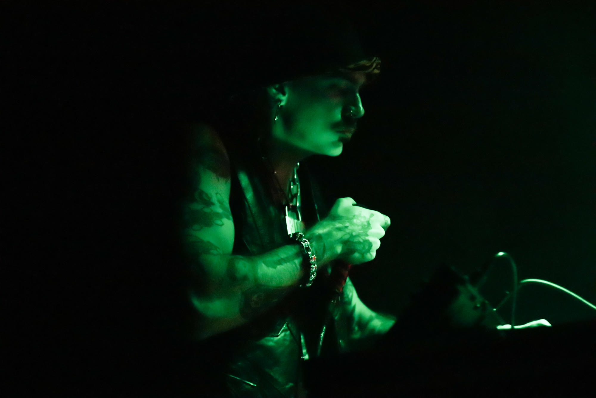 Performer in profile under green stage light, hands clasped around a microphone