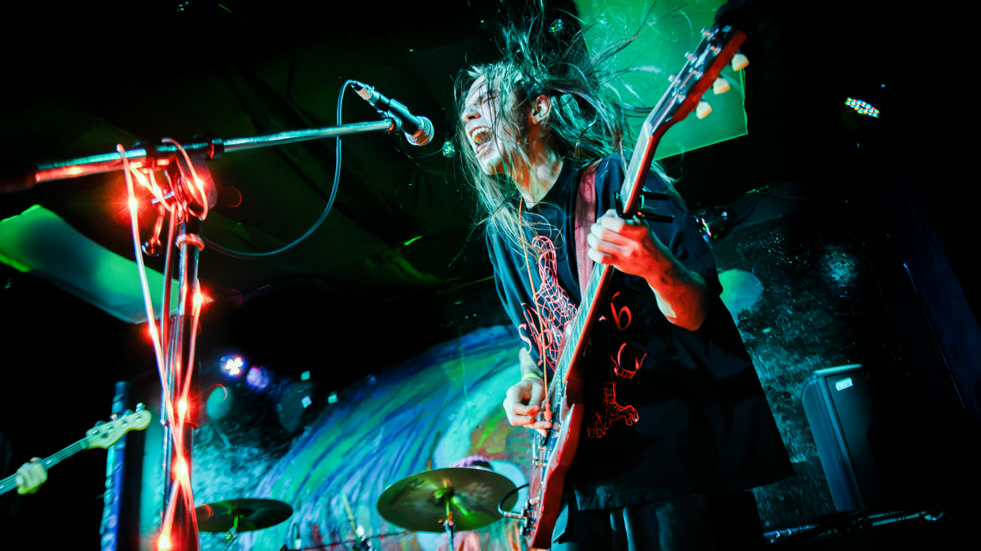 Guitarist with long hair plays and sings under green stage light