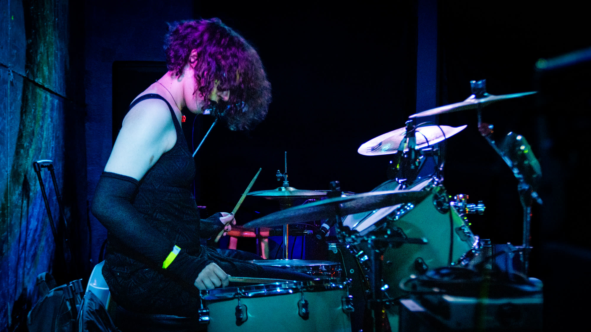 Drummer with curly hair plays under purple stage light