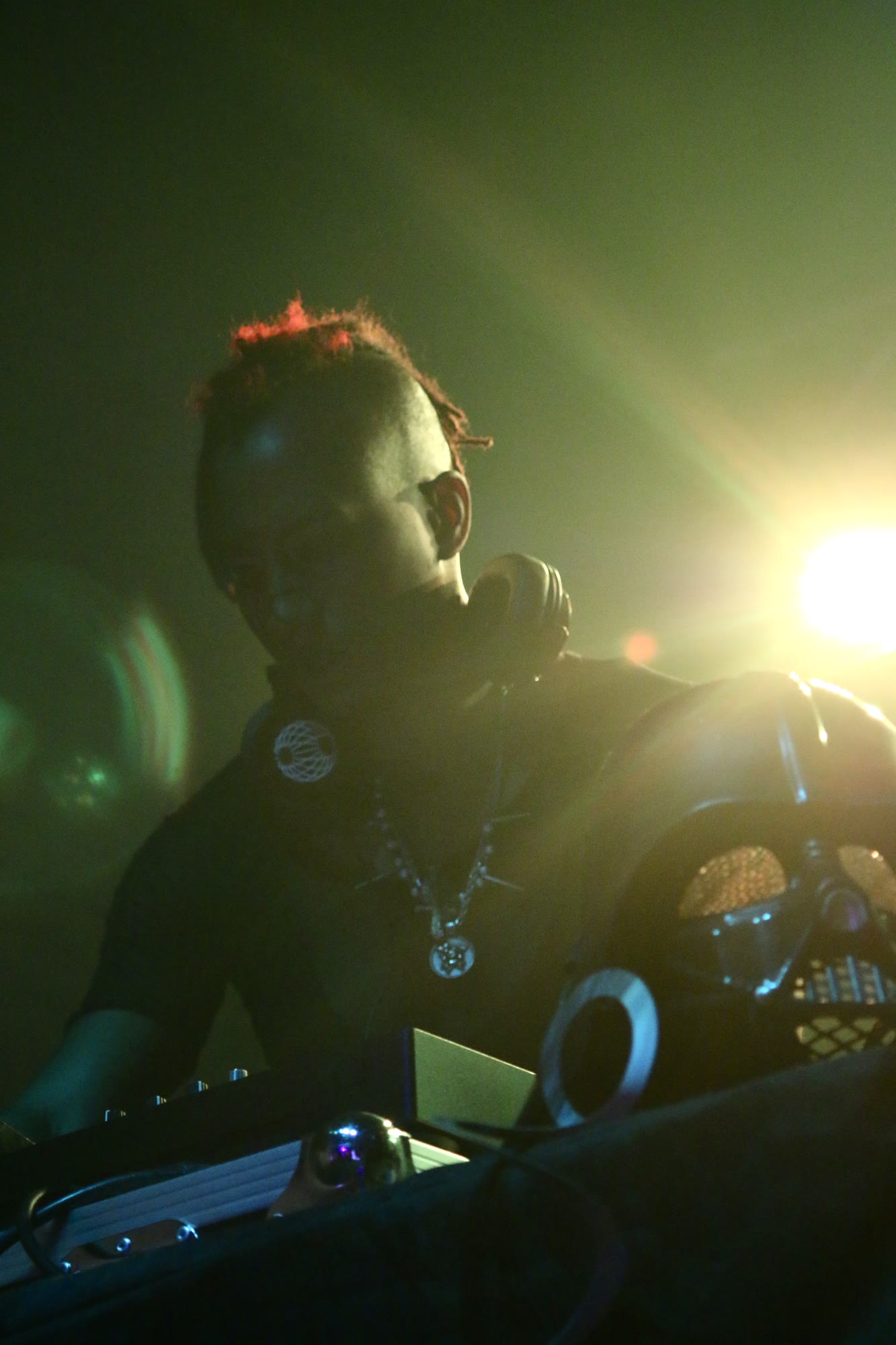 DJ with a red mohawk and headphones works the decks under green light