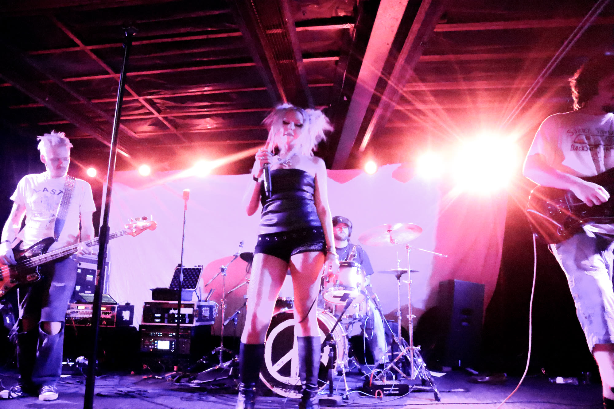 Band performs under red stage light, with a peace sign on the bass drum
