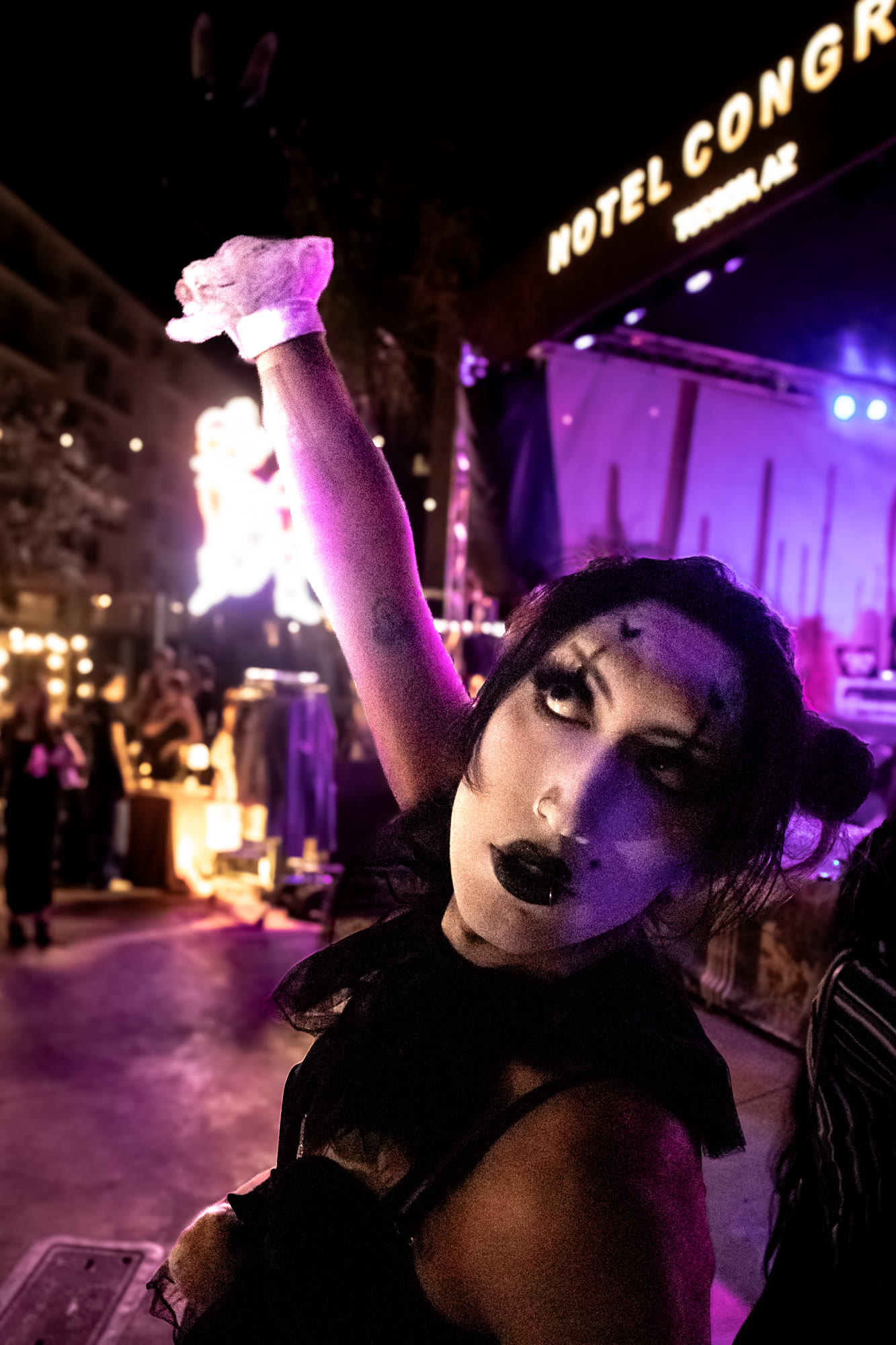 Performer with dark makeup raises an arm in front of the Hotel Congress sign in Tucson
