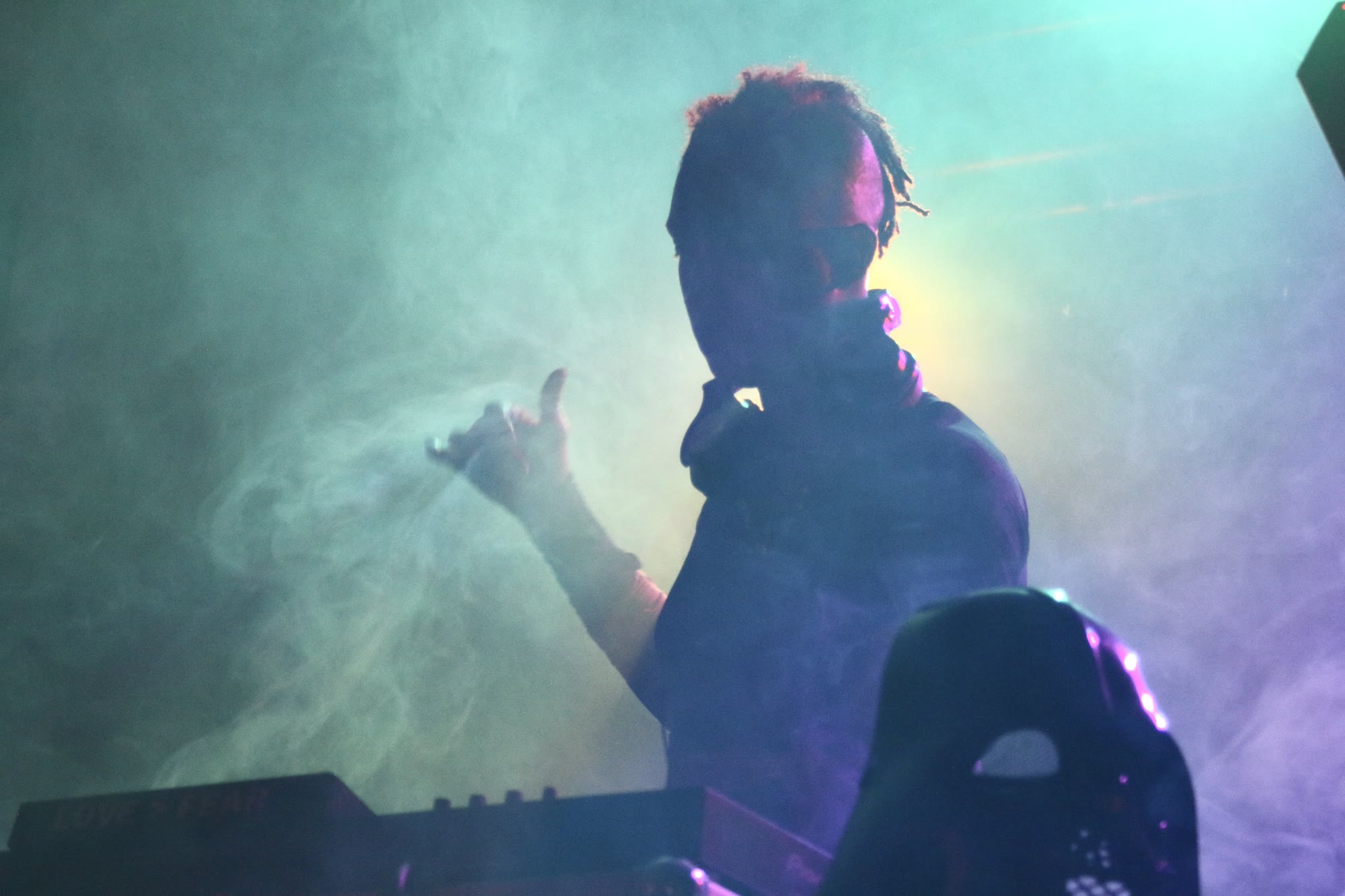 Musician in stage haze raises a hand above the keys, headphones around their neck