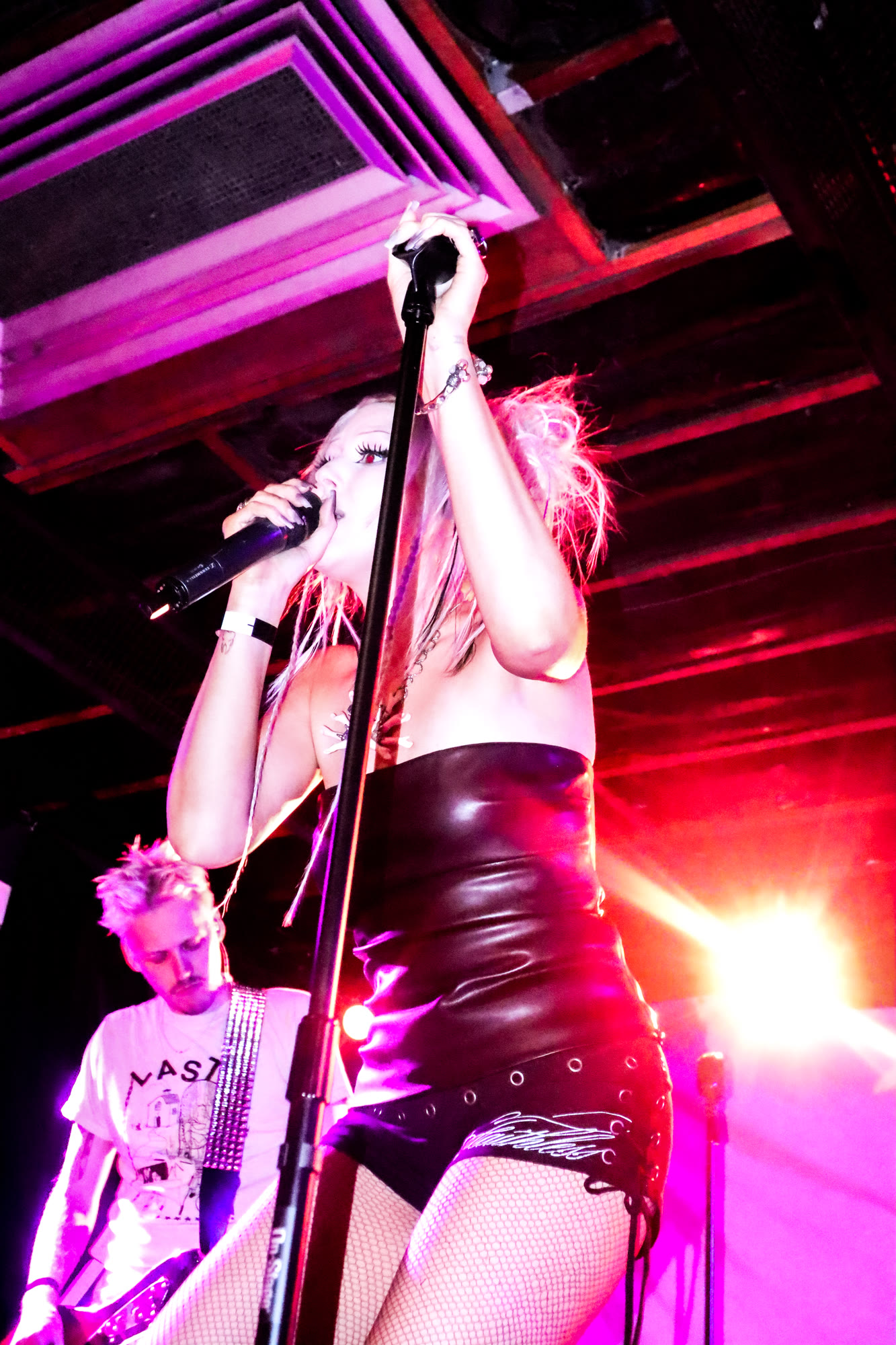 Singer in black holds a microphone with both hands under pink and red light