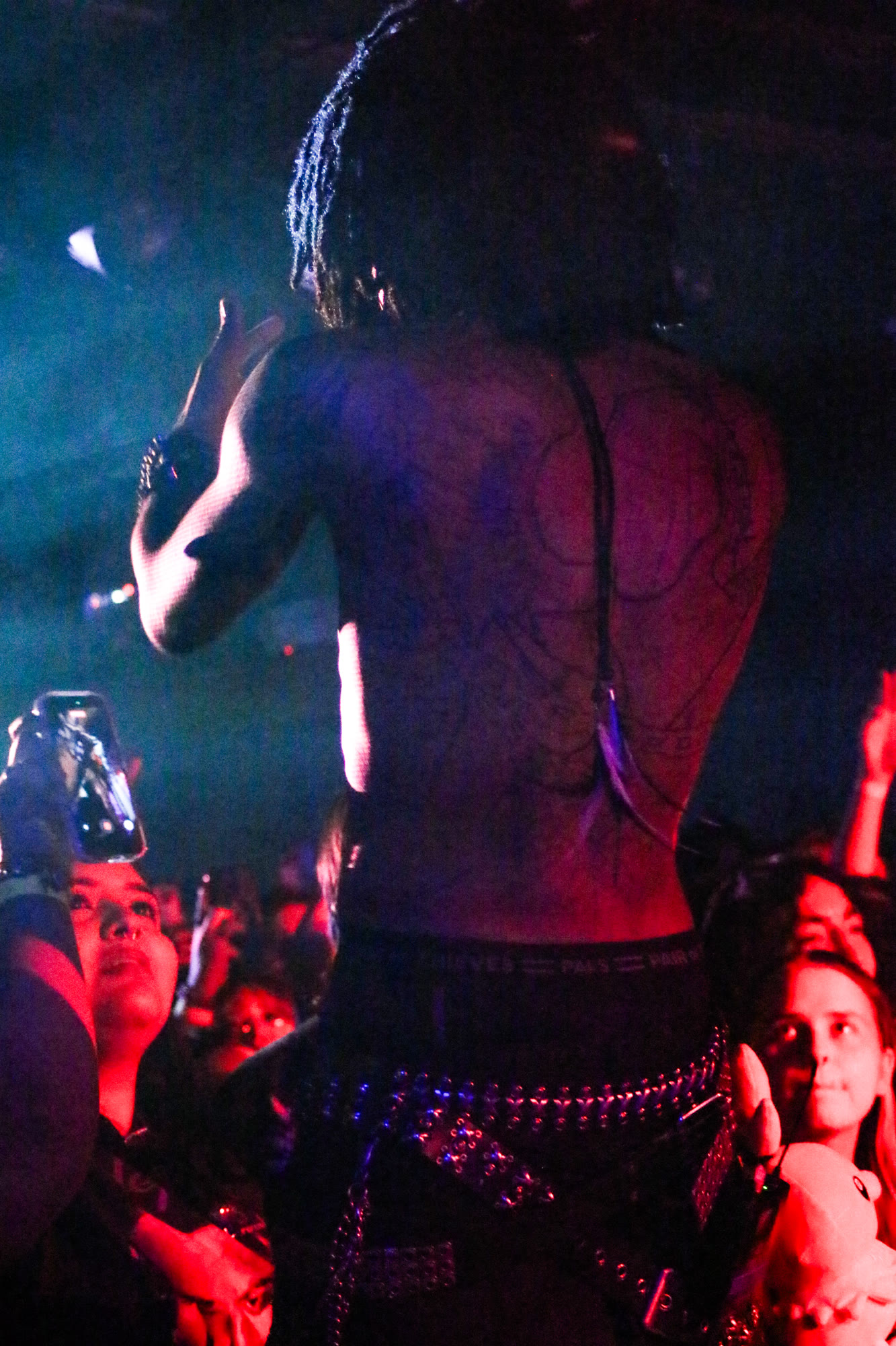 Performer faces the crowd, back and tattoos visible under red and blue light