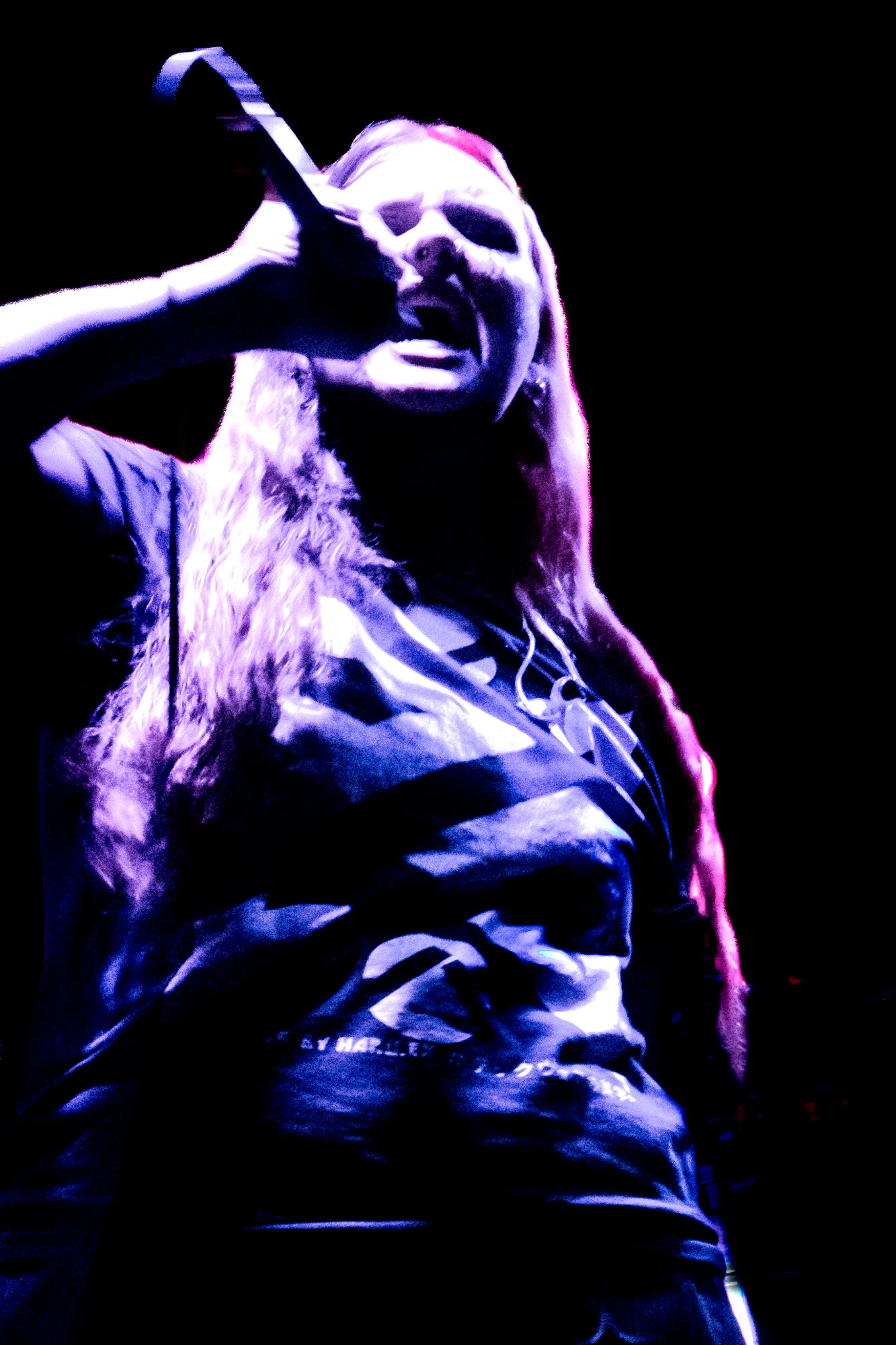 Singer with long hair sings into a microphone under purple light