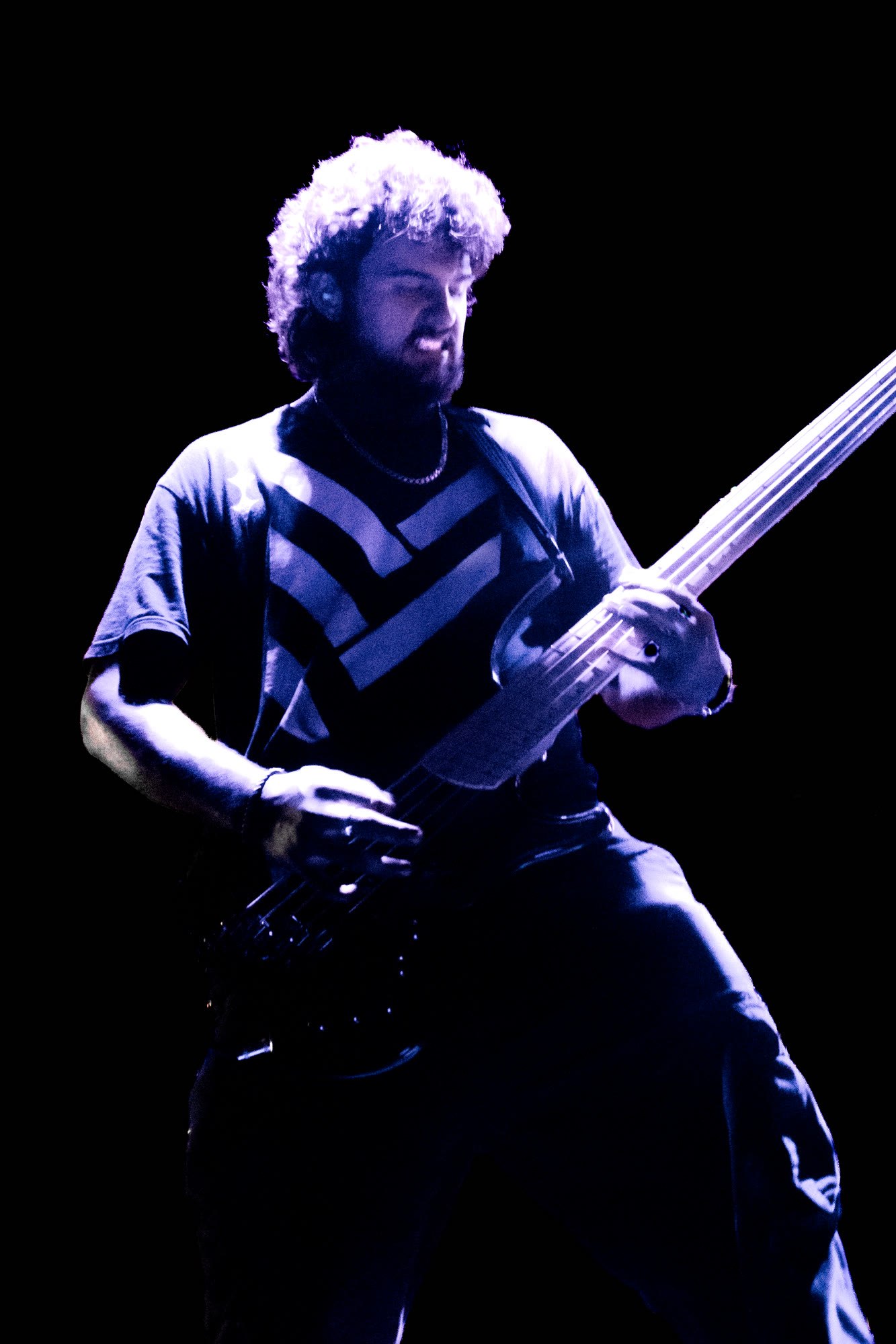 Bassist with curly hair plays under purple light